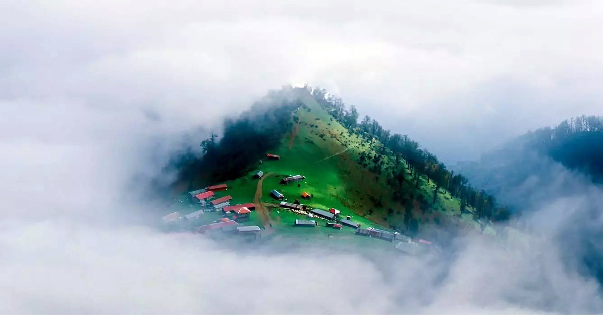 منظره زیبای ییلاق اولسبلنگاه در ماسال، گیلان، پوشیده شده از مه غلیظ و کلبه‌های چوبی روستایی که حس آرامش و زیبایی طبیعت را منتقل می‌کند.